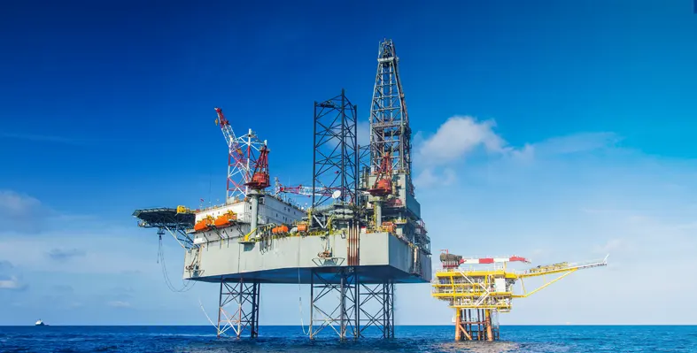 Oil rig in the sea with smaller rig in the background against blue sky