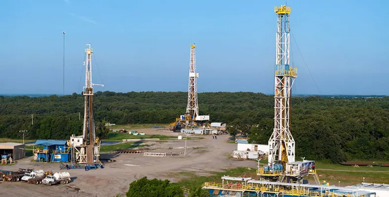 Three drilling rigs against a blue sky and green trees