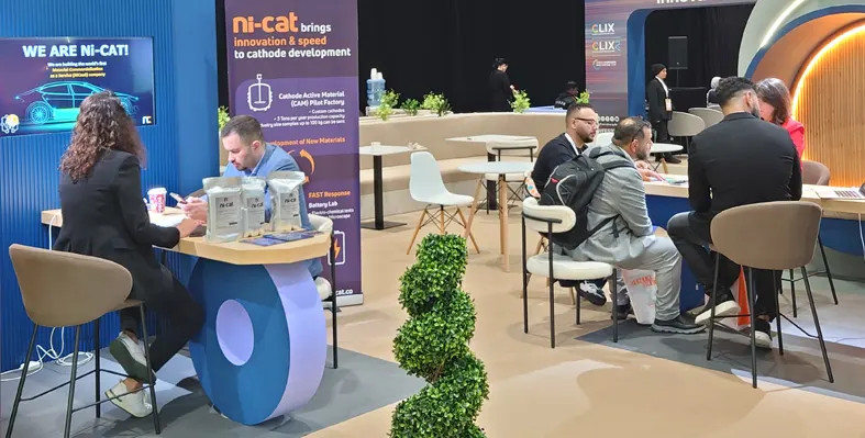 Men and women sitting at desks at trade show with company banners in the background